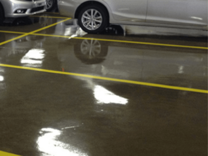 Vagas de estacionamento com piso epóxi brilhante e demarcações amarelas, com carros estacionados sobre o revestimento.