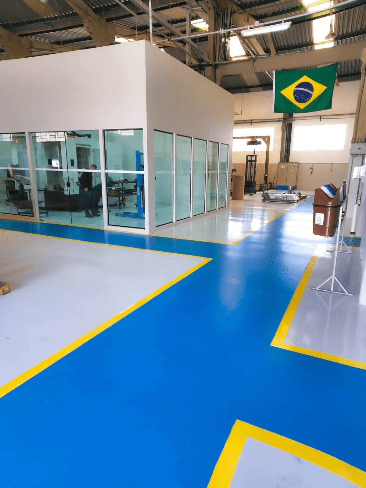 Piso epóxi azul e cinza com faixas amarelas em ambiente fabril.