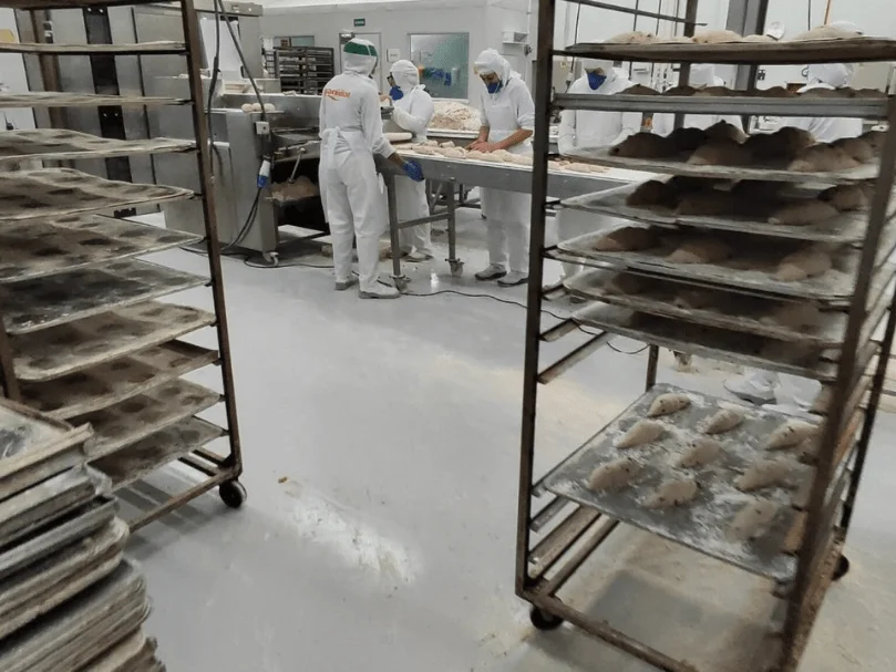 Área de produção alimentícia com piso epóxi cinza e equipe trabalhando em mesa de preparo.